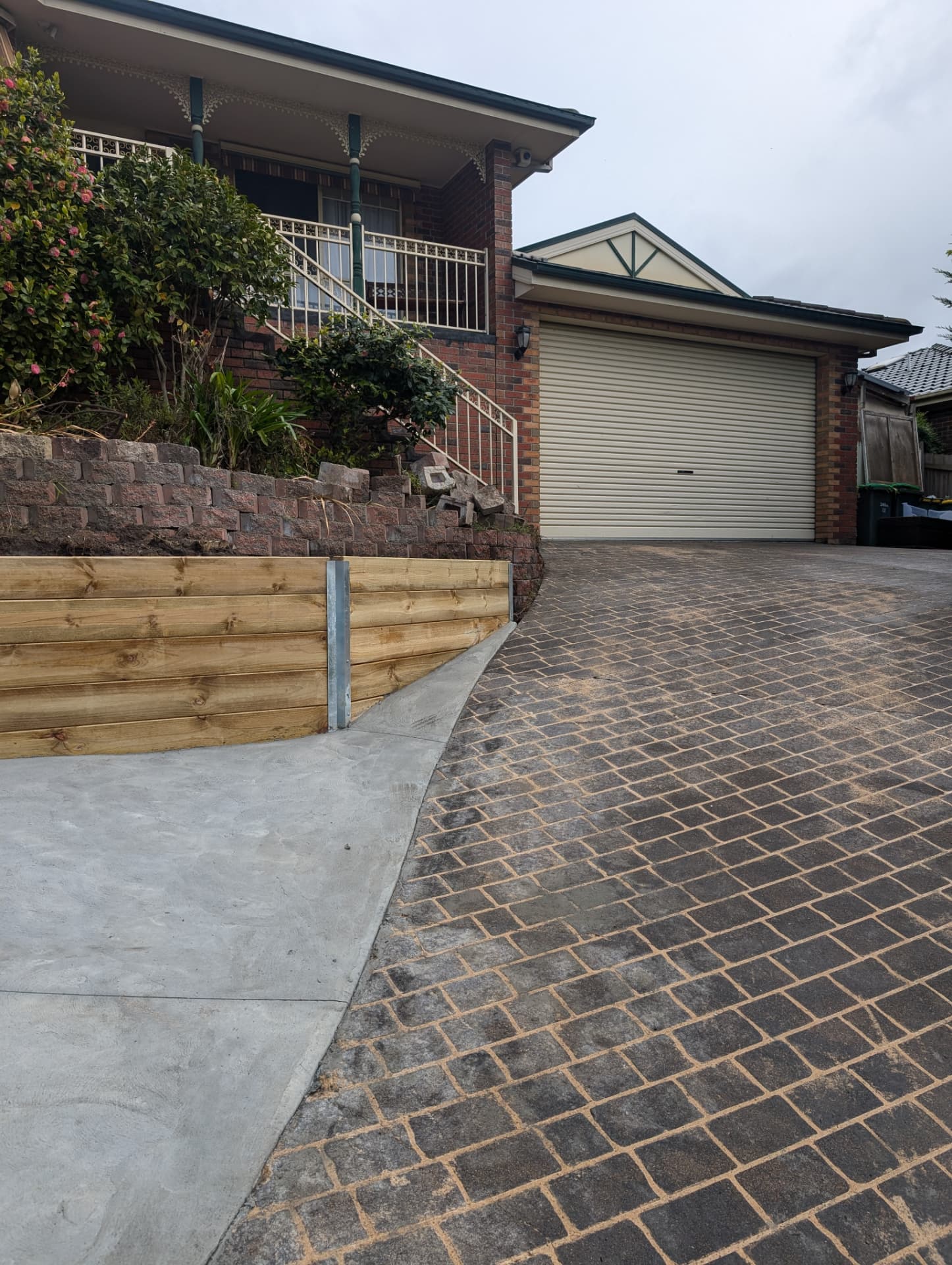 Timber sleeper retaining wall beside a paved driveway and concrete path