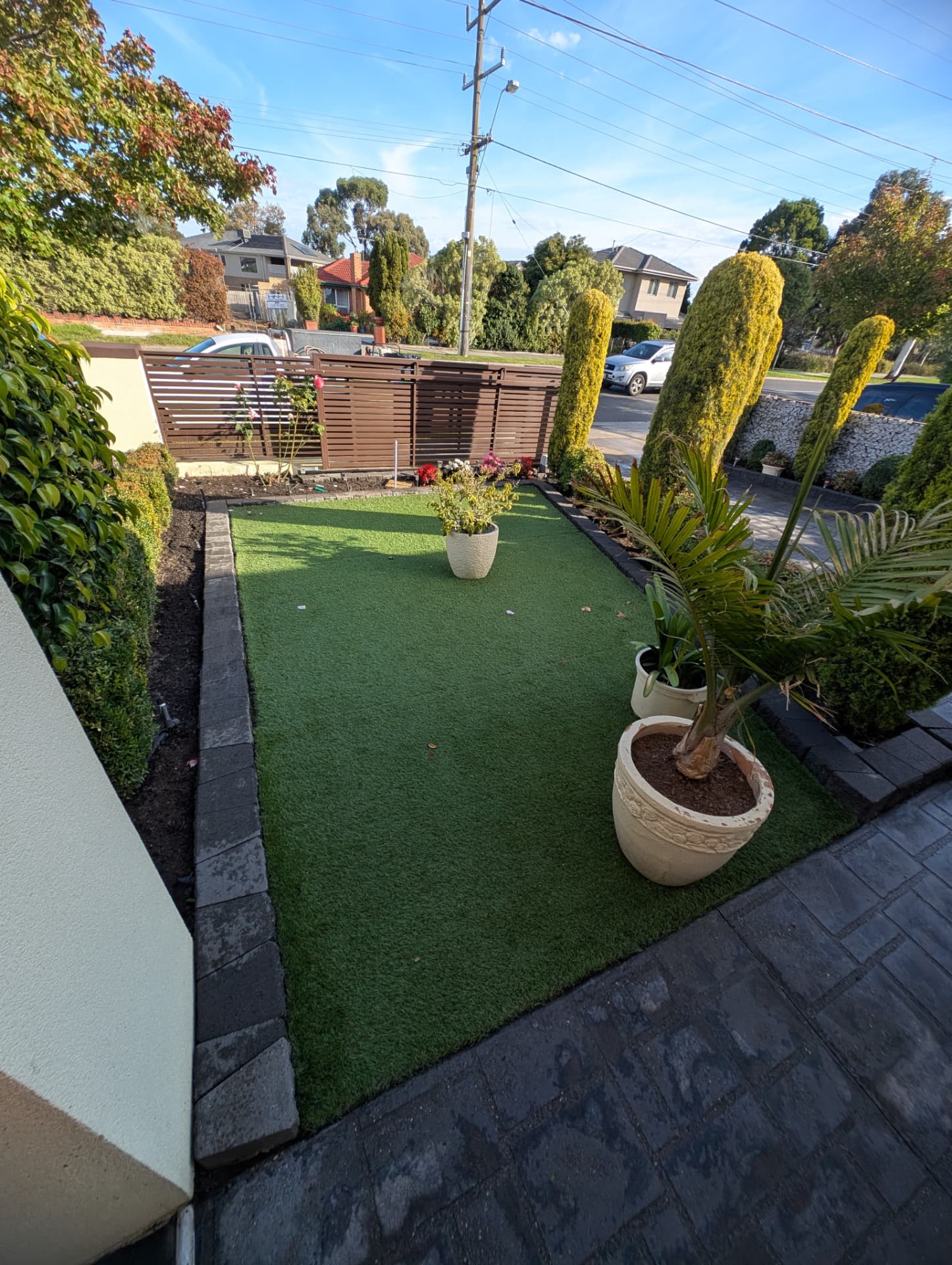 Front yard with synthetic turf, bluestone edging, garden beds and slat fencing